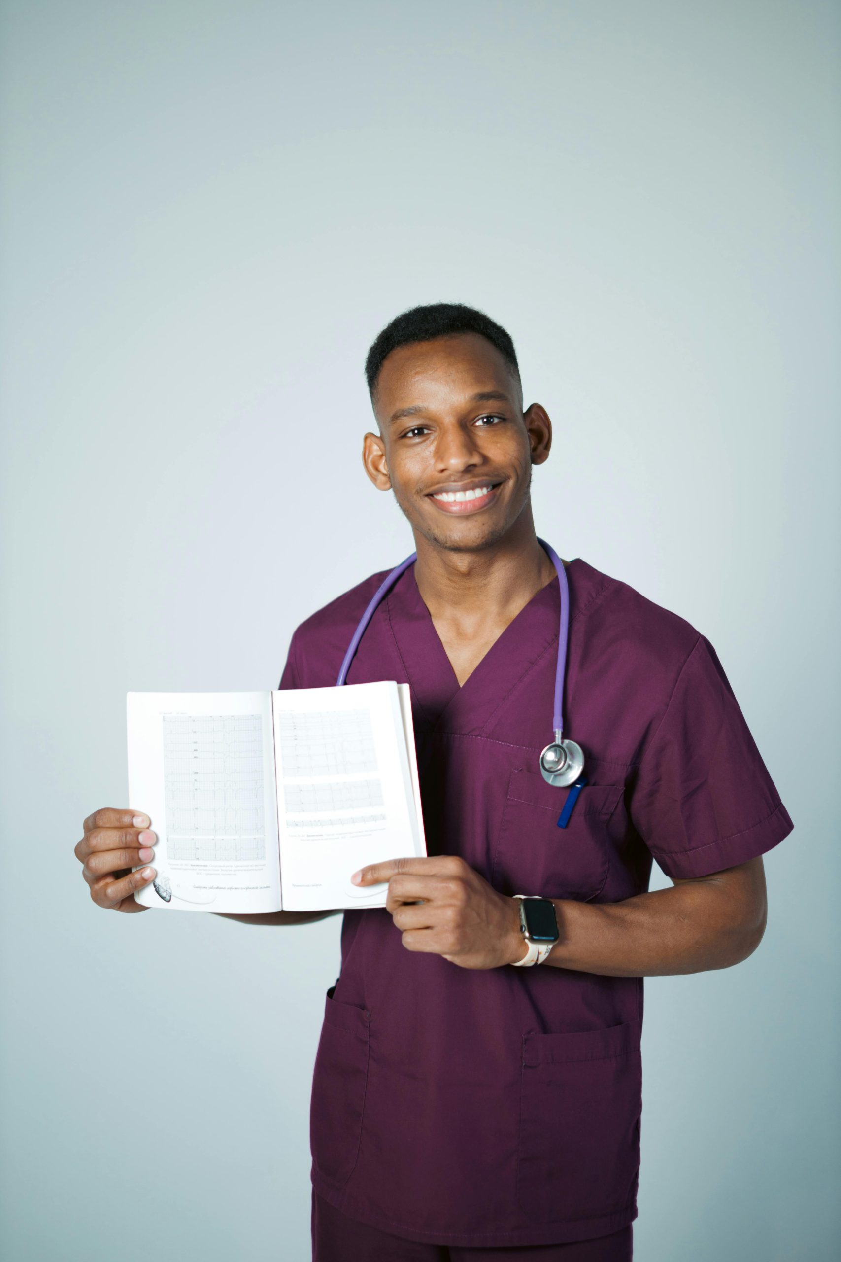 Smiling male nurse holding an open book with a stethoscope around his neck, promoting healthcare education.